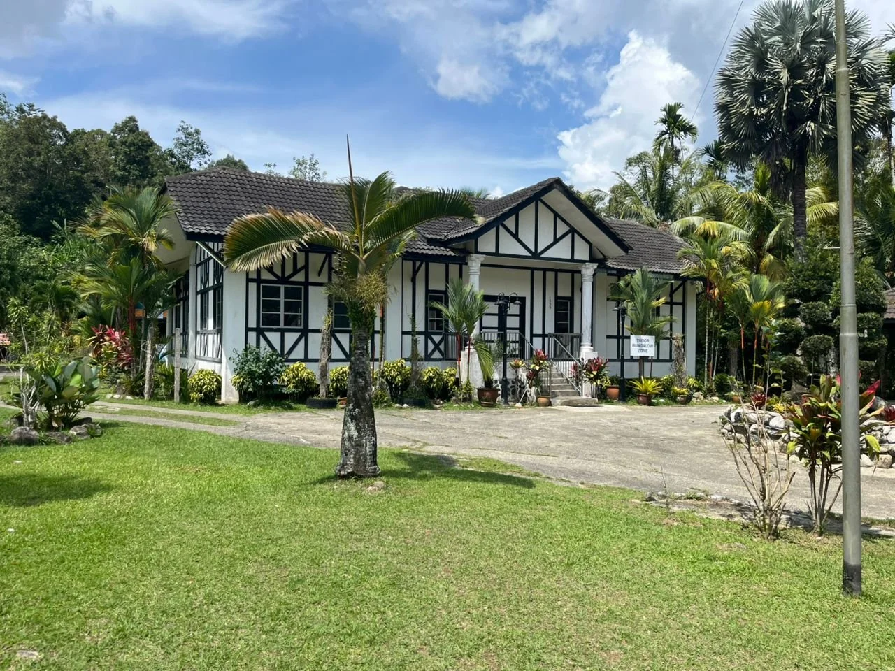 Le' Manah's black-and-white Tudor bungalow on a green lawn, with forested hills behind